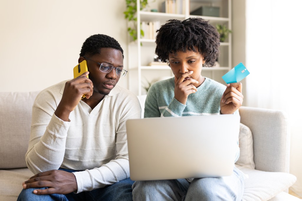 Worried couple at home using a laptop and credit card while dealing with an online payment problem