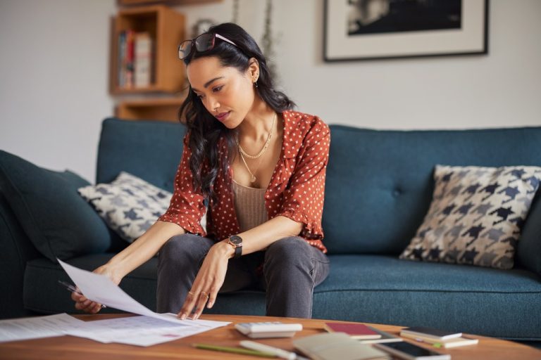 Woman sitting on a couch at home reading a paper statement